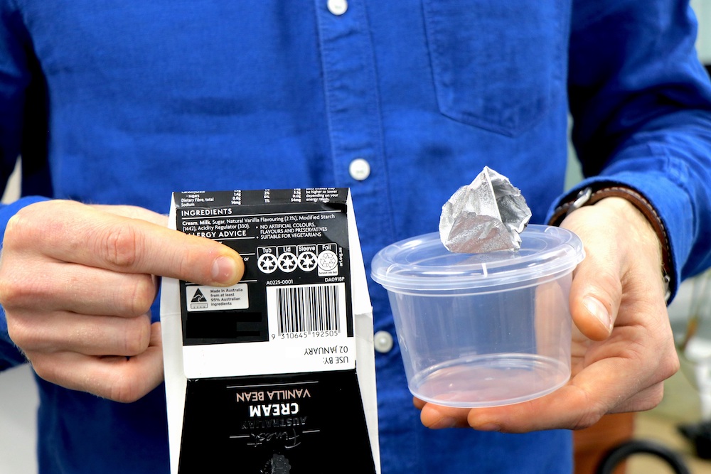 A person points to recycling instructions on a carton while holding separated packaging components.